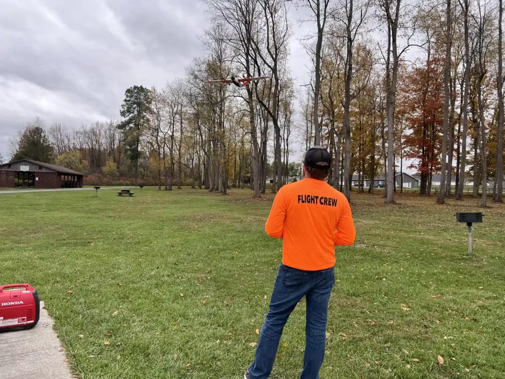 Harkin flight crew member in an orange shirt flying a drone over a park