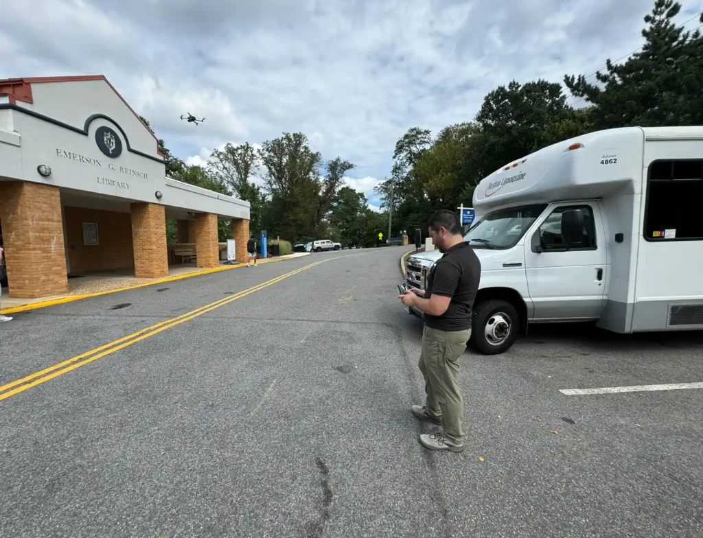 Harkin pilot with a controller in front of a campus library while a drone flies overhead