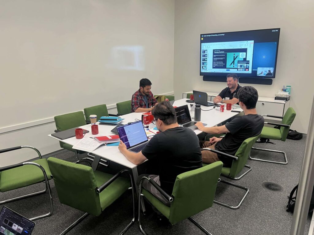Training class around a table with laptops and wall display