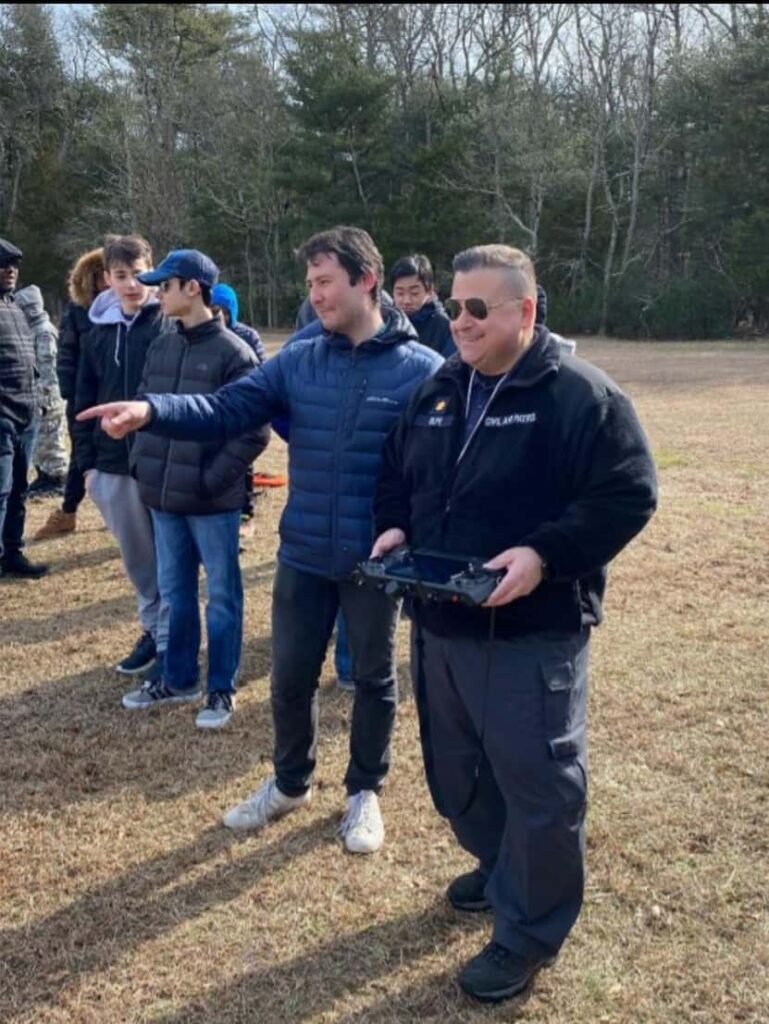 Instructor and students outdoors watching a drone flight with controller