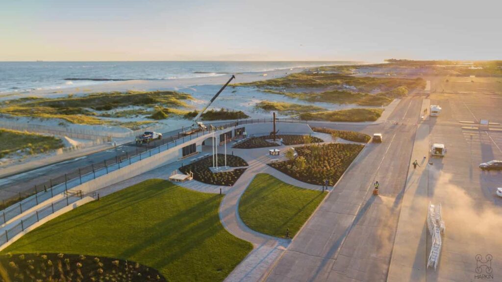 Drone photo of a waterfront site at sunset with lawn, paved paths and a construction crane