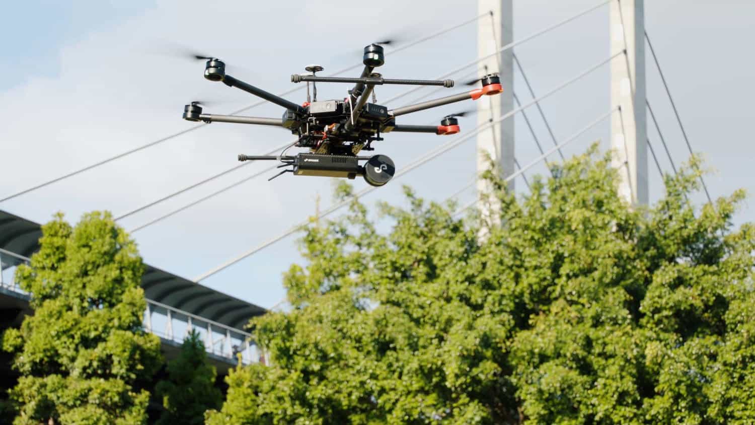 Harkin drone carrying a LIDAR scanner, flying near trees and a bridge