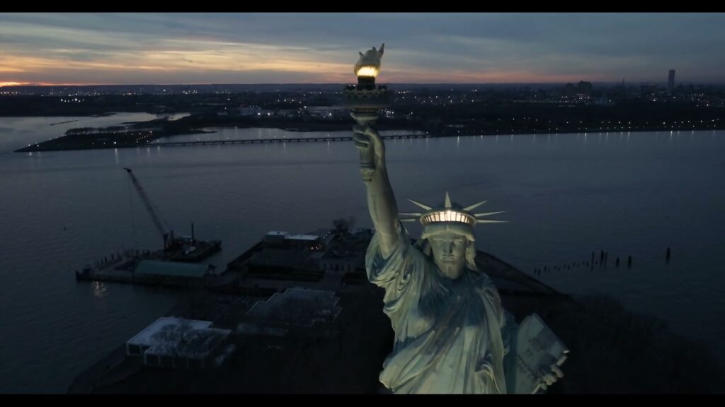 Drone view of the Statue of Liberty at dusk with the torch lit above New York Harbor